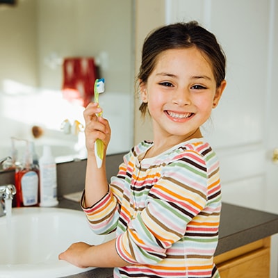 A little girl in front of a mirror smiling while holding a yellow toothbrush