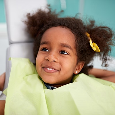 A little girl wearing a small yellow ribbon while get top pediatric dental services