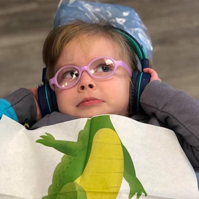 A little girl lying down while wearing headphones and pink glasses