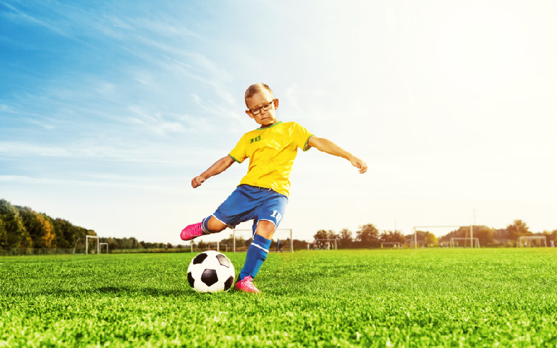 young boy kicking soccer ball outside