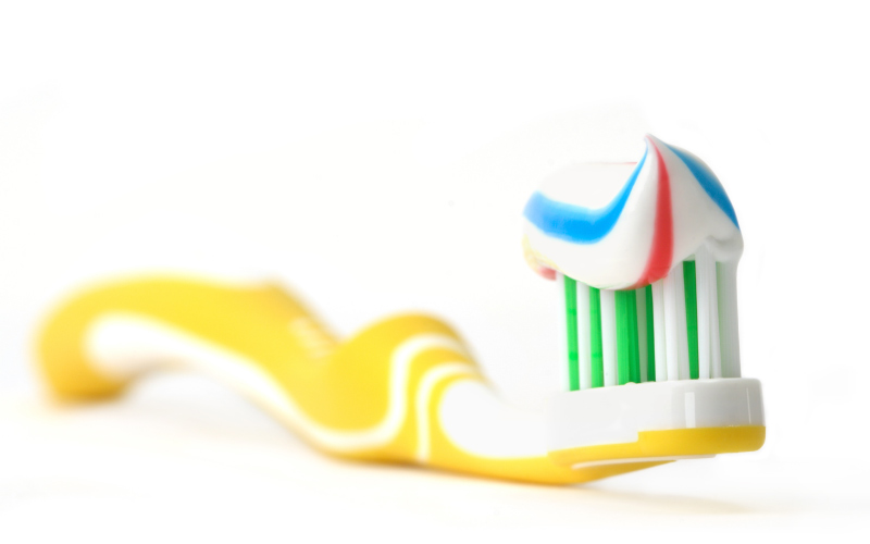 yellow toothbrush with blue red and white striped toothpaste sitting on white counter