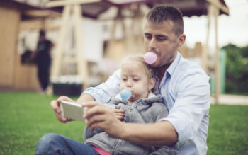 Father and young daughter outside blowing bubbles with chewing gum and taking a picture